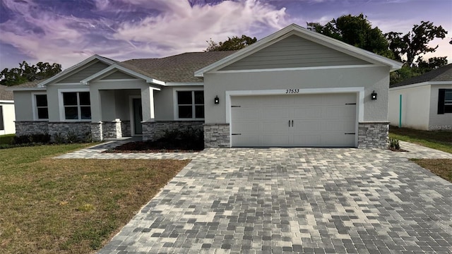 craftsman-style home featuring a garage, a lawn, decorative driveway, stone siding, and stucco siding
