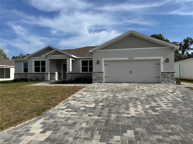 craftsman house with decorative driveway, a front yard, stone siding, and stucco siding