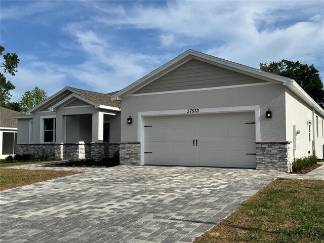 craftsman inspired home with a garage, stucco siding, decorative driveway, and stone siding