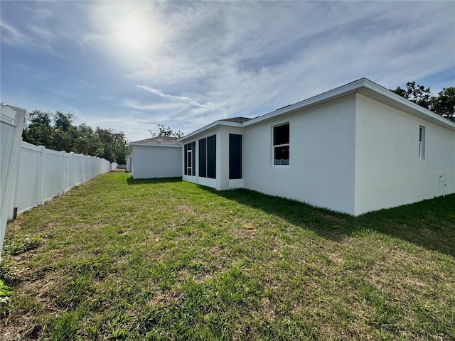 back of house featuring stucco siding, fence, and a lawn