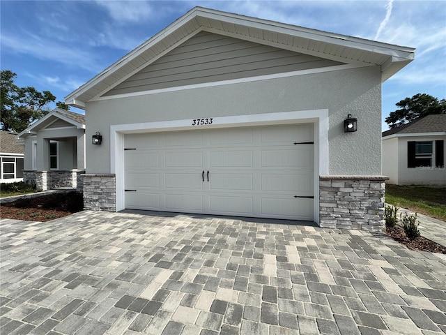 view of front of home featuring stucco siding, decorative driveway, and stone siding