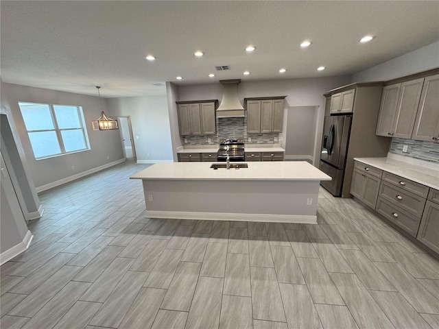 kitchen featuring appliances with stainless steel finishes, a center island with sink, decorative backsplash, and custom range hood