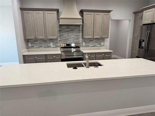 kitchen featuring a sink, backsplash, light stone counters, premium range hood, and appliances with stainless steel finishes
