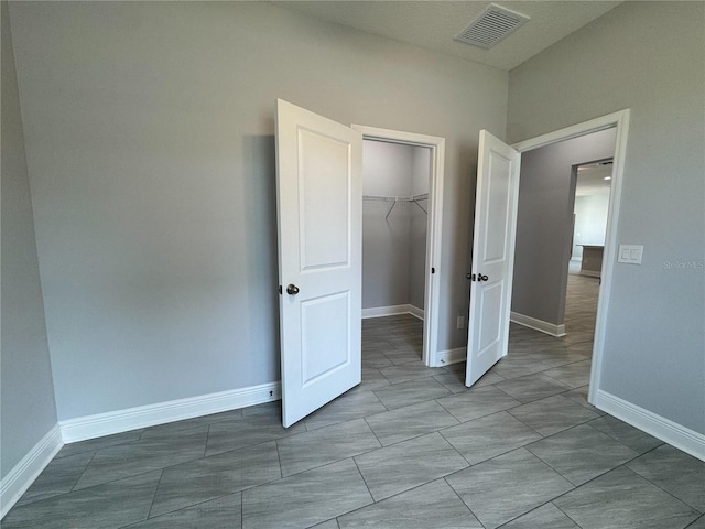 unfurnished bedroom featuring visible vents, a closet, baseboards, and a walk in closet