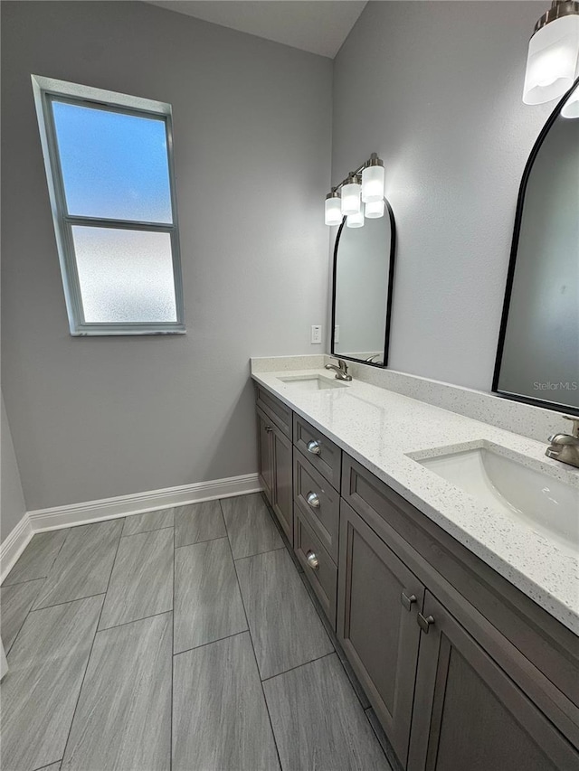 full bath featuring baseboards, double vanity, and a sink