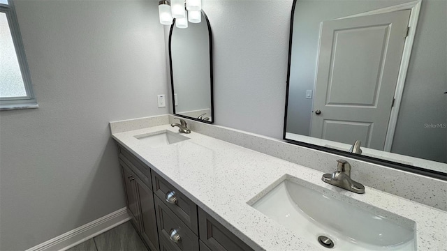 full bathroom with baseboards, double vanity, and a sink
