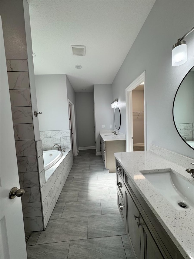 full bath with a spacious closet, two vanities, a bath, and a sink