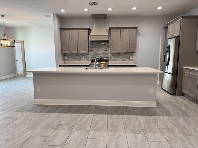 kitchen with an island with sink, stainless steel appliances, light countertops, a sink, and premium range hood