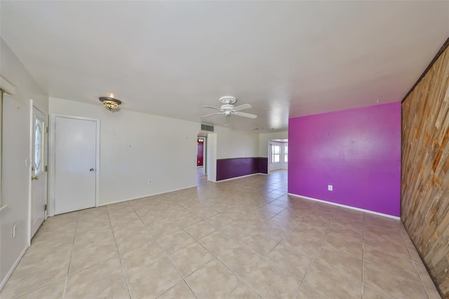 spare room with light tile patterned floors, a ceiling fan, wood walls, and visible vents