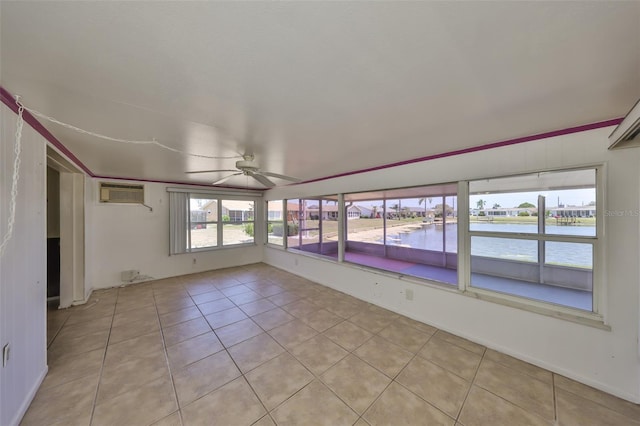 unfurnished sunroom featuring a ceiling fan, tile patterned floors, a wall unit AC, and a water view