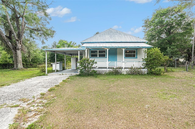 country-style home featuring covered porch, a front yard, gravel driveway, an attached carport, and metal roof