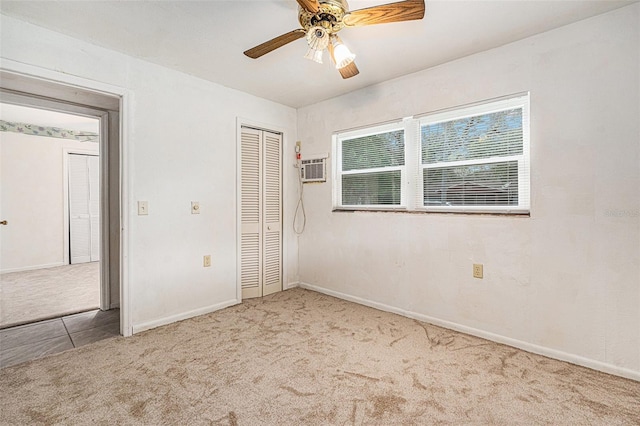 unfurnished bedroom with a closet, baseboards, a wall unit AC, a ceiling fan, and carpet