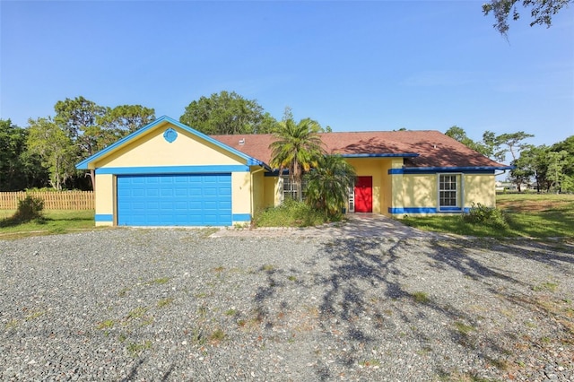 ranch-style house with an attached garage, fence, stucco siding, and gravel driveway