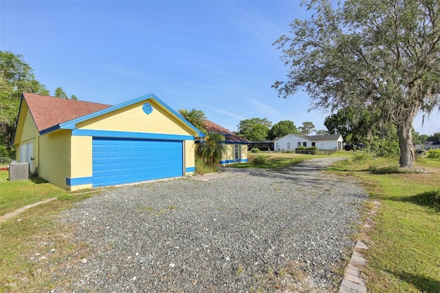 view of side of property featuring stucco siding, a garage, a lawn, and central AC