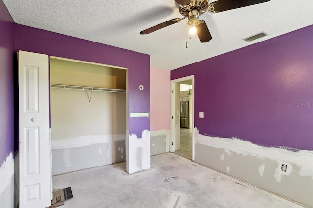 unfurnished bedroom with a closet, freestanding refrigerator, visible vents, ceiling fan, and a textured ceiling