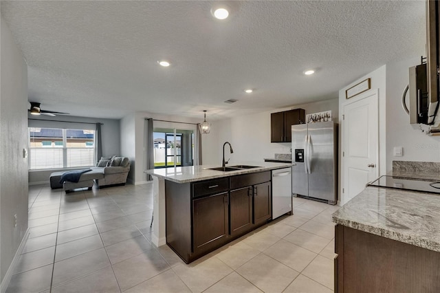 kitchen featuring stainless steel appliances, a sink, dark brown cabinets, open floor plan, and a kitchen island with sink