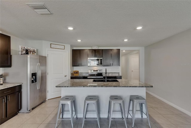 kitchen featuring a sink, stainless steel appliances, a kitchen breakfast bar, light tile patterned flooring, and recessed lighting