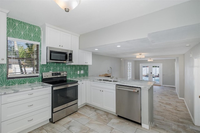 kitchen with appliances with stainless steel finishes, tasteful backsplash, a sink, a peninsula, and white cabinetry