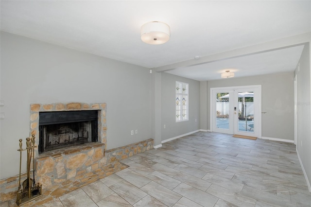 unfurnished living room featuring baseboards, a stone fireplace, and french doors