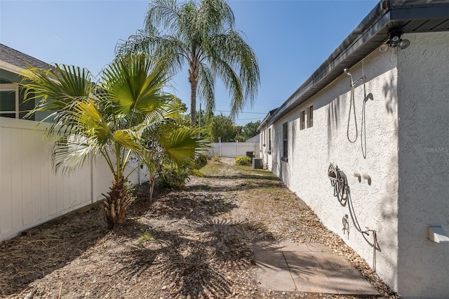 view of side of home with a fenced backyard, stucco siding, and central AC