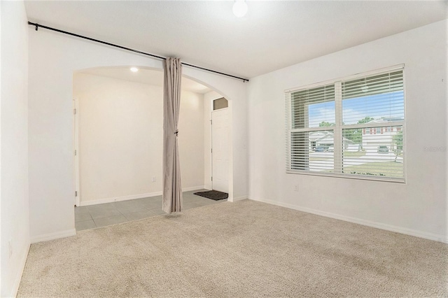unfurnished bedroom featuring baseboards, arched walkways, carpet floors, and tile patterned flooring