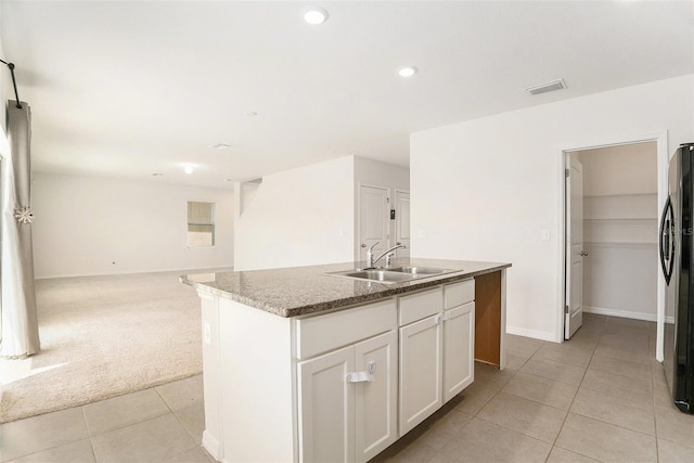 kitchen with a sink, light tile patterned floors, visible vents, freestanding refrigerator, and light colored carpet