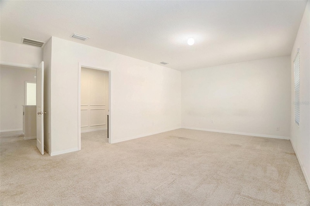 unfurnished room with visible vents, light carpet, and baseboards