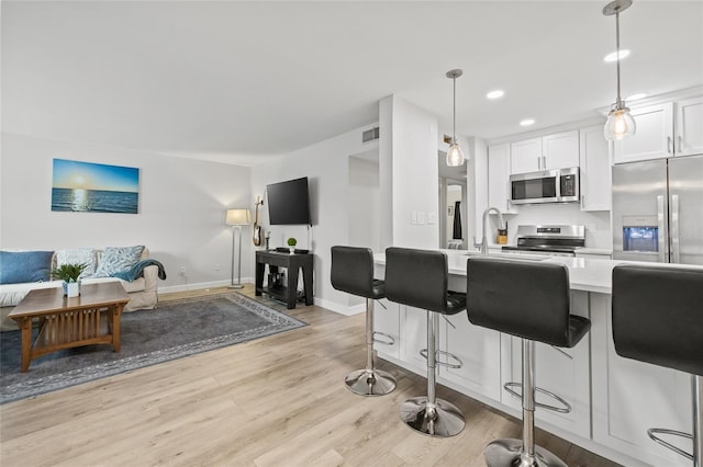 kitchen featuring appliances with stainless steel finishes, light countertops, white cabinetry, open floor plan, and a kitchen bar