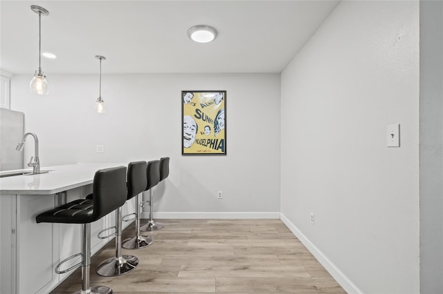 bar featuring a sink, light wood finished floors, freestanding refrigerator, baseboards, and pendant lighting