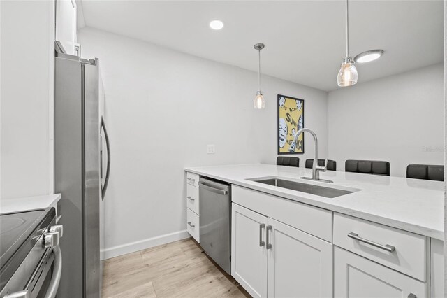 kitchen with light wood-style floors, white cabinets, a sink, appliances with stainless steel finishes, and hanging light fixtures