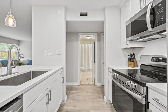 kitchen with appliances with stainless steel finishes, a sink, light countertops, light wood-style floors, and white cabinetry