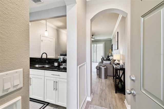 bar featuring arched walkways, a sink, light wood finished floors, ornamental molding, and a textured wall