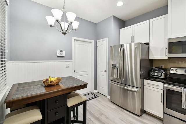 kitchen featuring wainscoting, white cabinets, a chandelier, light wood finished floors, and stainless steel appliances