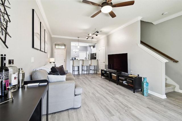living area with crown molding, a ceiling fan, light wood finished floors, and stairway