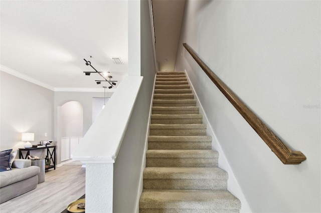 stairway with crown molding, arched walkways, wood finished floors, and visible vents