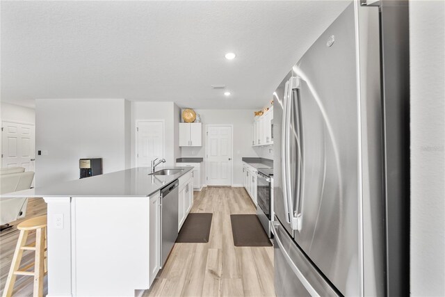 7797 Peace Lily Ave, Wesley Chapel, FL 33545 - kitchen featuring appliances with stainless steel finishes, white cabinets, light wood finished floors, a sink, and a center island with sink