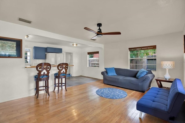 living room with visible vents, wood finished floors, and a ceiling fan