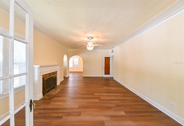 unfurnished living room featuring arched walkways, a textured ceiling, a ceiling fan, a fireplace with flush hearth, and ornamental molding
