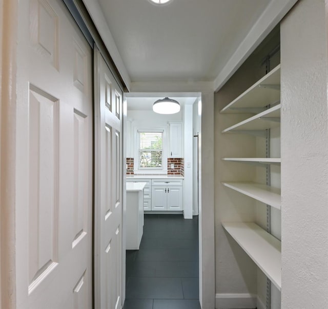 corridor with dark tile patterned flooring and baseboards