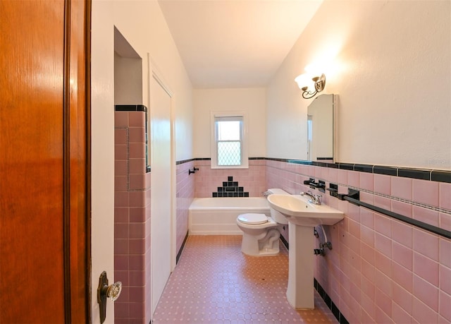 bathroom with wainscoting, a sink, toilet, tile walls, and a tub to relax in