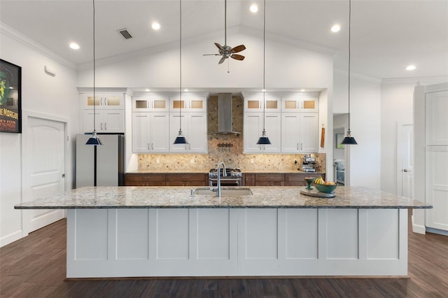 kitchen with wall chimney range hood, appliances with stainless steel finishes, a sink, white cabinetry, and visible vents