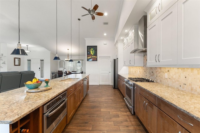 kitchen featuring a sink, dark wood-style flooring, wall chimney range hood, a ceiling fan, and appliances with stainless steel finishes