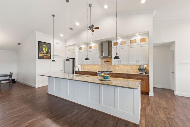 kitchen with wall chimney exhaust hood, stainless steel appliances, a large island, a ceiling fan, and vaulted ceiling