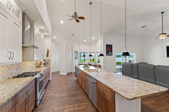 kitchen with a sink, open floor plan, wall chimney range hood, a ceiling fan, and stainless steel appliances