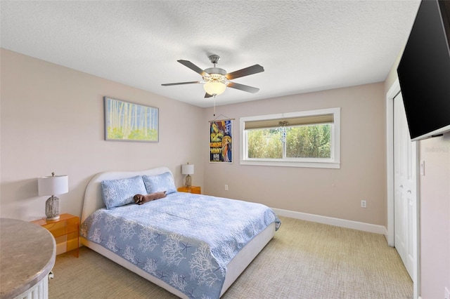 bedroom featuring light colored carpet, a textured ceiling, a ceiling fan, baseboards, and a closet