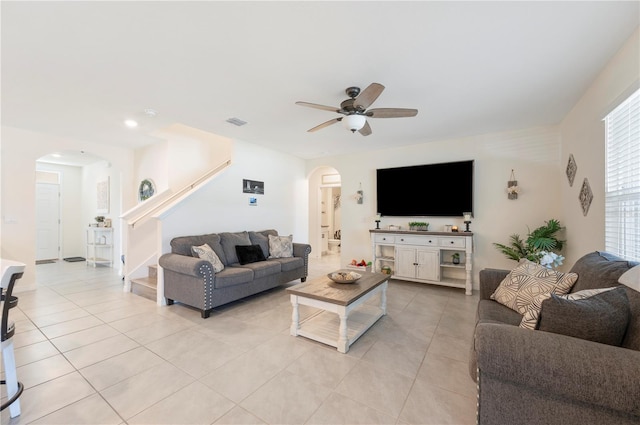 living room with visible vents, a ceiling fan, stairs, arched walkways, and light tile patterned floors