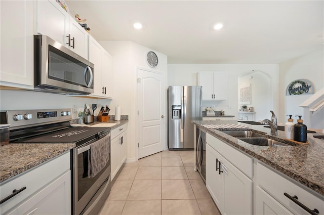 kitchen featuring white cabinets, stainless steel appliances, a sink, and dark stone countertops