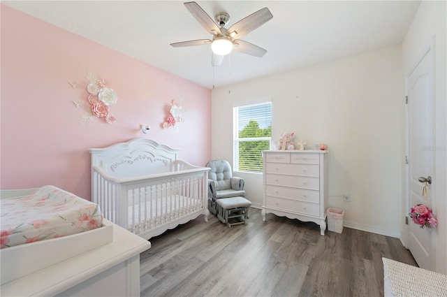 bedroom featuring a crib, baseboards, a ceiling fan, and wood finished floors