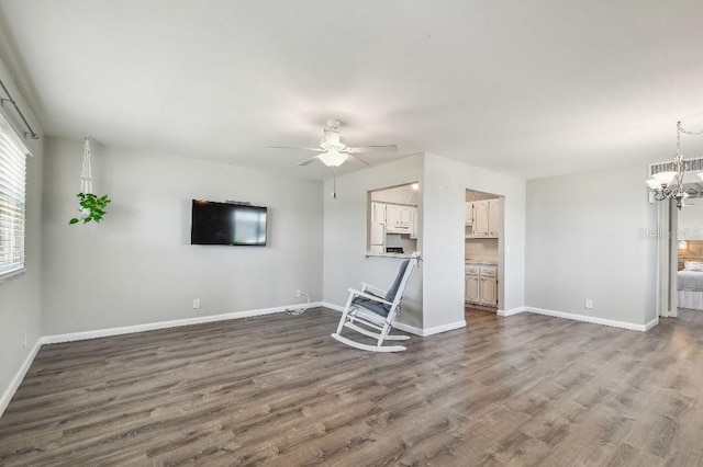 unfurnished living room with ceiling fan with notable chandelier, baseboards, dark wood-type flooring, and visible vents
