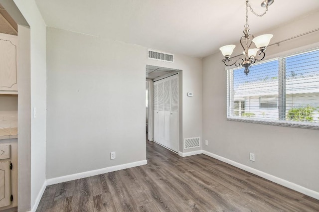 unfurnished dining area featuring a notable chandelier, baseboards, visible vents, and wood finished floors